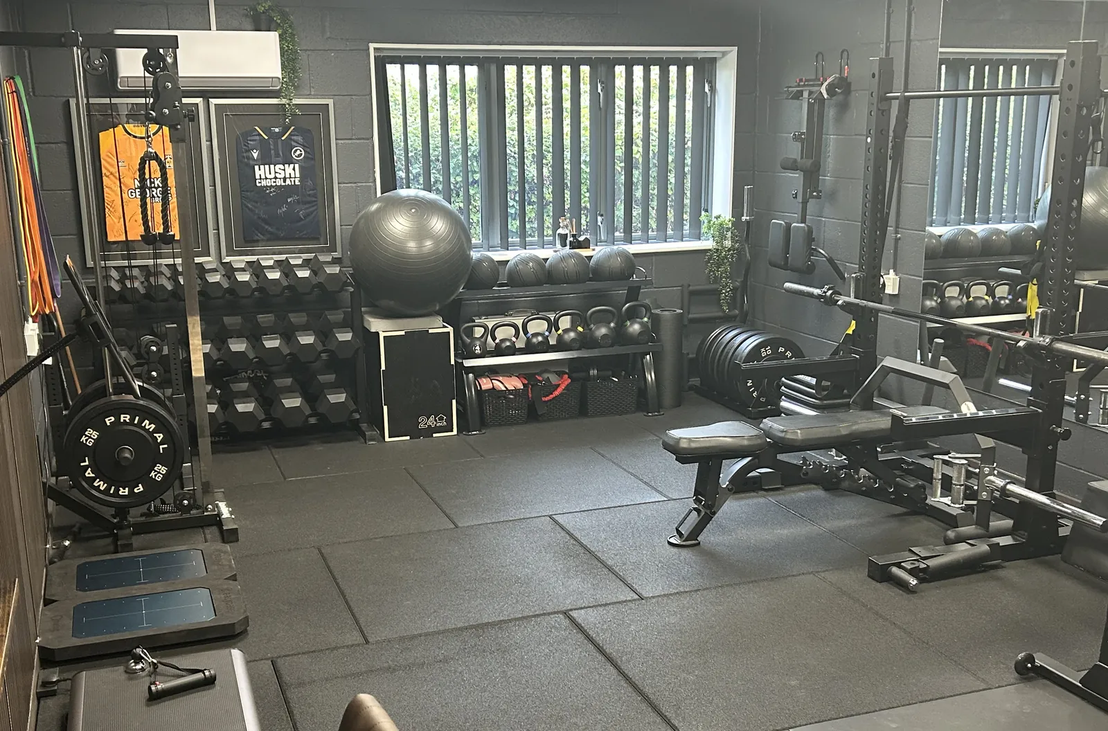 Strength training area at Elite Health & Performance, with a power rack, bench, dumbbells and framed match shirts